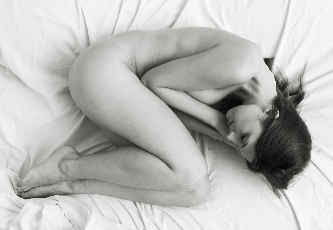 femme nue recroquevillée sur elle même sur un lit